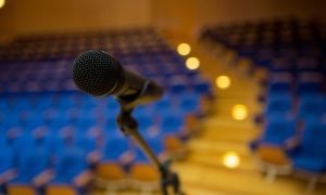 Micrófono en primer plano listo para ponencia motivacional en auditorio con asientos azules